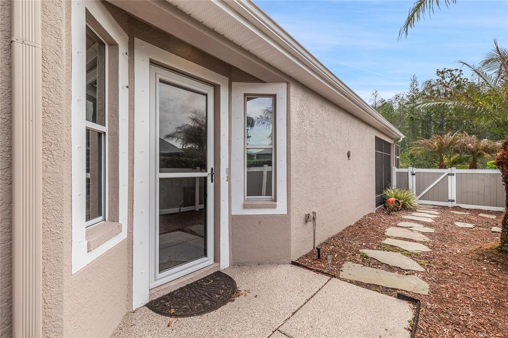 A beige stucco house exterior features a glass storm door, windows, and a stone walkway — 8328 PONKAN ROAD, LAND O LAKES, FL