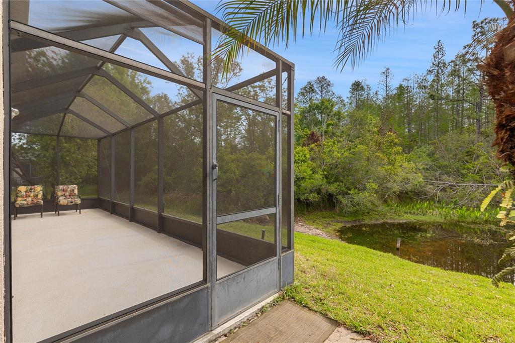 A screened-in patio with two chairs overlooks a grassy yard and a small pond — 8328 PONKAN ROAD, LAND O LAKES, FL