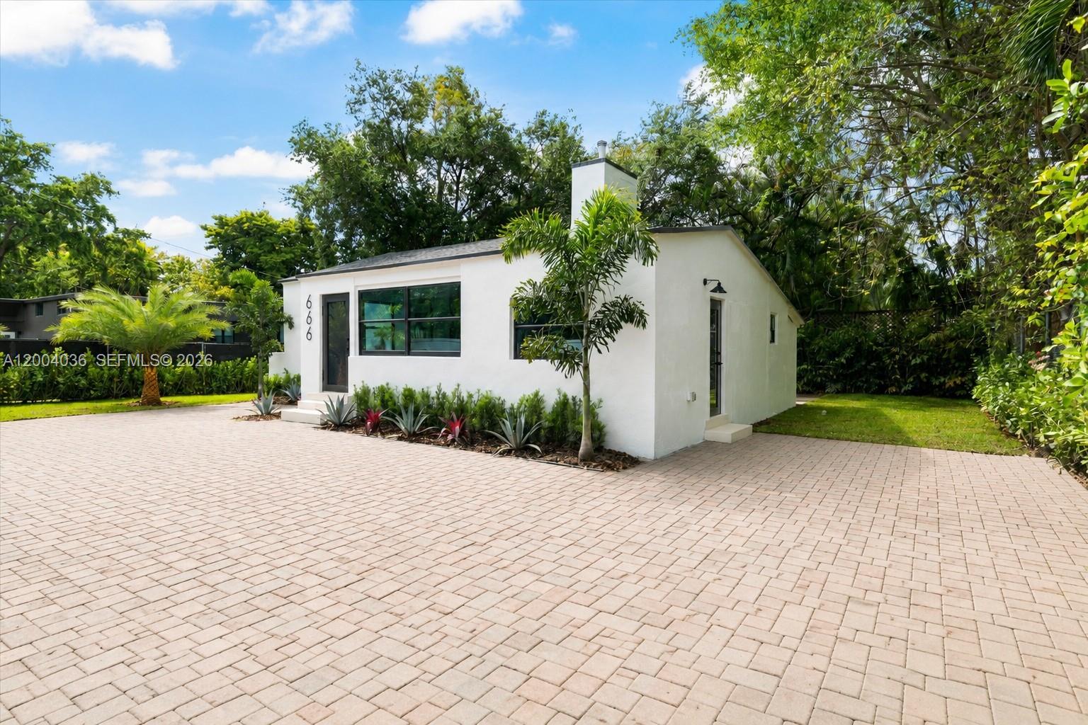A white, single-story house with a paved driveway and landscaping sits under a blue sky — 666 NE 62nd St, Miami FL 33138, MIAMI, FL