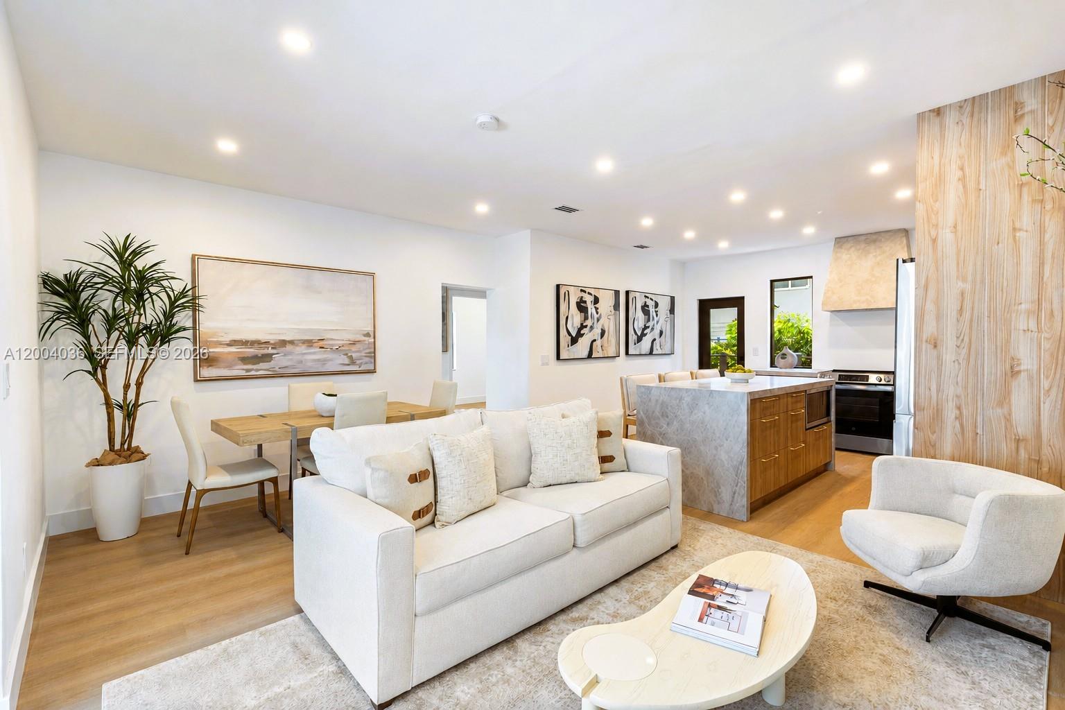 This open-concept living and dining area features light wood floors, a marble island, and neutral furniture — 666 NE 62nd St, Miami FL 33138, MIAMI, FL