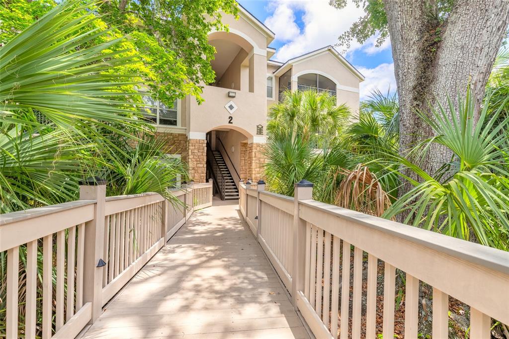 A wooden footbridge leads to the entrance of a multi-story apartment building with stone accents — 940 VILLAGE TRAIL UNIT 2-208, PORT ORANGE, FL