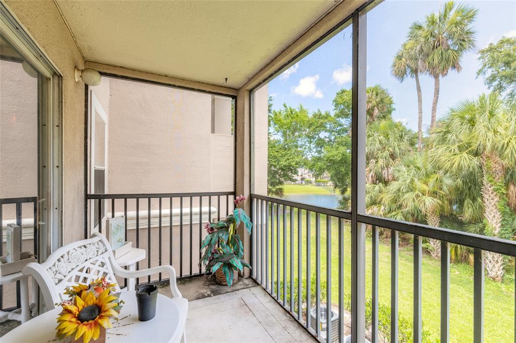 A screened-in balcony features a white table, chairs, and a view of palm trees — 940 VILLAGE TRAIL UNIT 2-208, PORT ORANGE, FL