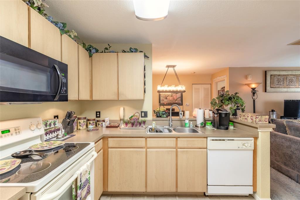 A kitchen with light wood cabinets, white appliances, and a view into the living area — 940 VILLAGE TRAIL UNIT 2-208, PORT ORANGE, FL