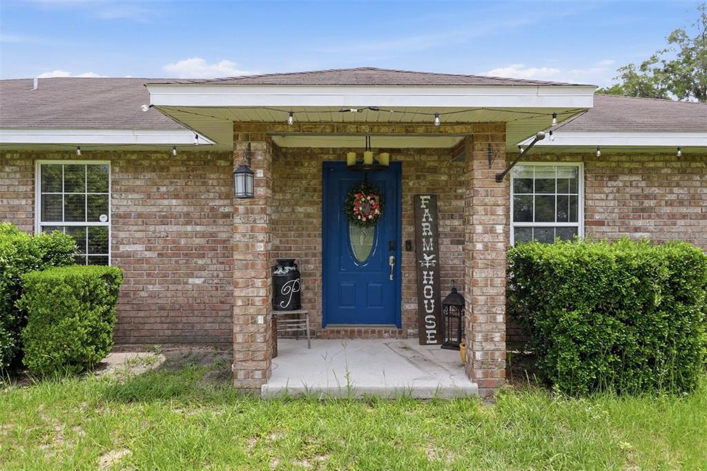 A brick house exterior features a blue front door with a wreath and porch lights — 3460 SE COUNTY ROAD 337, TRENTON, FL
