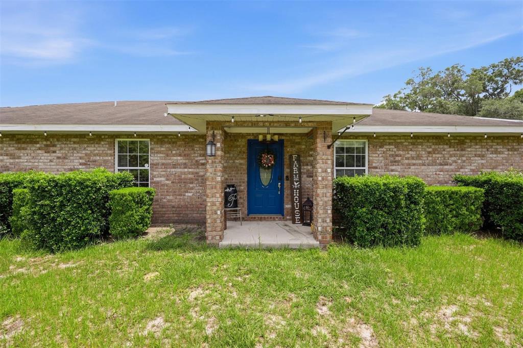 A single-story brick house features a blue front door under a covered porch entrance — 3460 SE COUNTY ROAD 337, TRENTON, FL