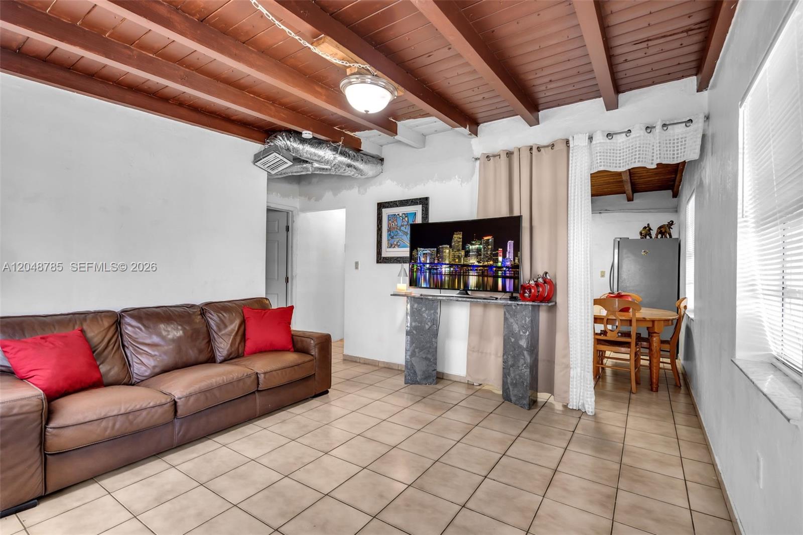 A living room features a brown leather sofa, tile flooring, and an exposed wood-beam ceiling — 6084 E 7th Ave, Hialeah FL 33013, HIALEAH, FL