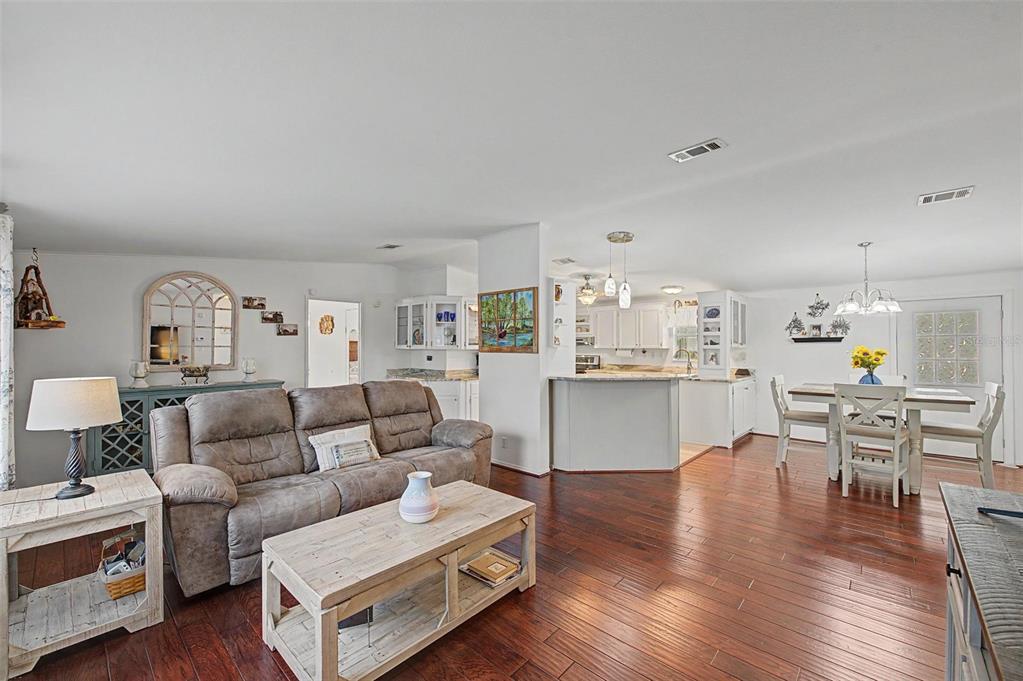 An open-concept living and dining area features dark wood floors, white cabinetry, and neutral furniture — 37719 NEWAL AVENUE, ZEPHYRHILLS, FL