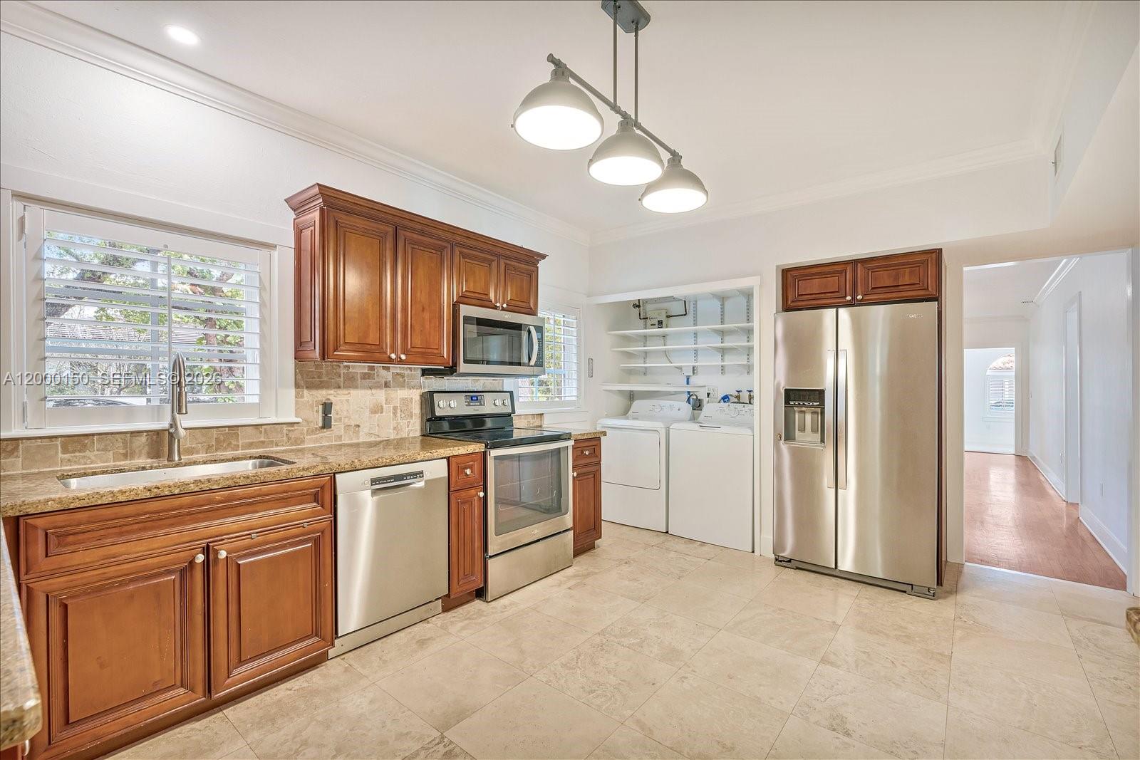 A kitchen features wood cabinets, stainless steel appliances, a tiled backsplash, and an open laundry area — 1102 Genoa St, Coral Gables FL 33134, CORAL GABLES, FL