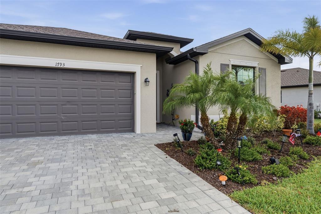 A single-story house with a gray garage door, paved driveway, and palm trees in front — 1793 SADDLEWOOD CIRCLE, PORT CHARLOTTE, FL