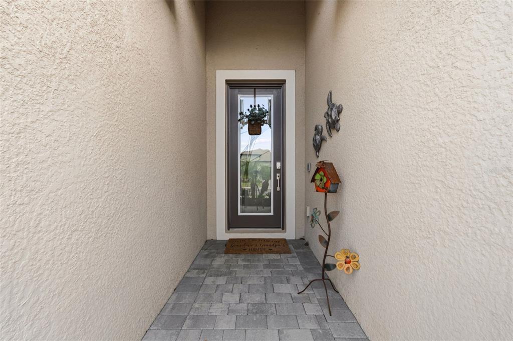 A covered entryway features a brown front door, stone pavers, and decorative wall-mounted turtle art — 1793 SADDLEWOOD CIRCLE, PORT CHARLOTTE, FL