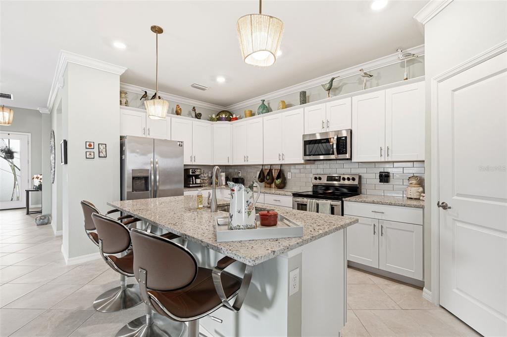 A kitchen features white cabinets, granite countertops, a center island with stools, and stainless appliances — 1793 SADDLEWOOD CIRCLE, PORT CHARLOTTE, FL