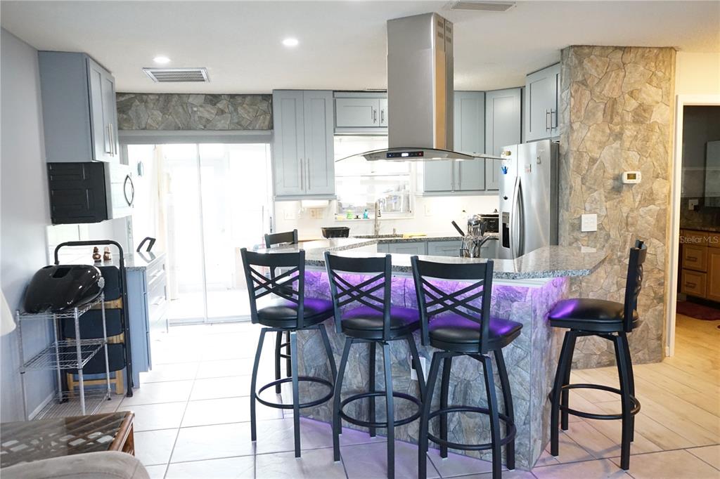 A kitchen features light blue cabinets, stone accents, a breakfast bar with stools, and stainless appliances — 424 LAKE POINT COURT UNIT 5A, SUN CITY CENTER, FL