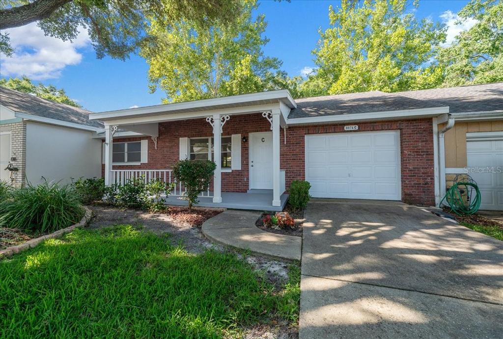 A single-story brick house features a covered front porch, a white door, and a garage — 8874 SW 95TH STREET UNIT C, OCALA, FL