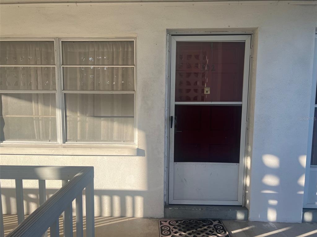 A white exterior wall features a window with curtains and a screen door entrance — 5155 9TH AVENUE N UNIT 302, ST PETERSBURG, FL