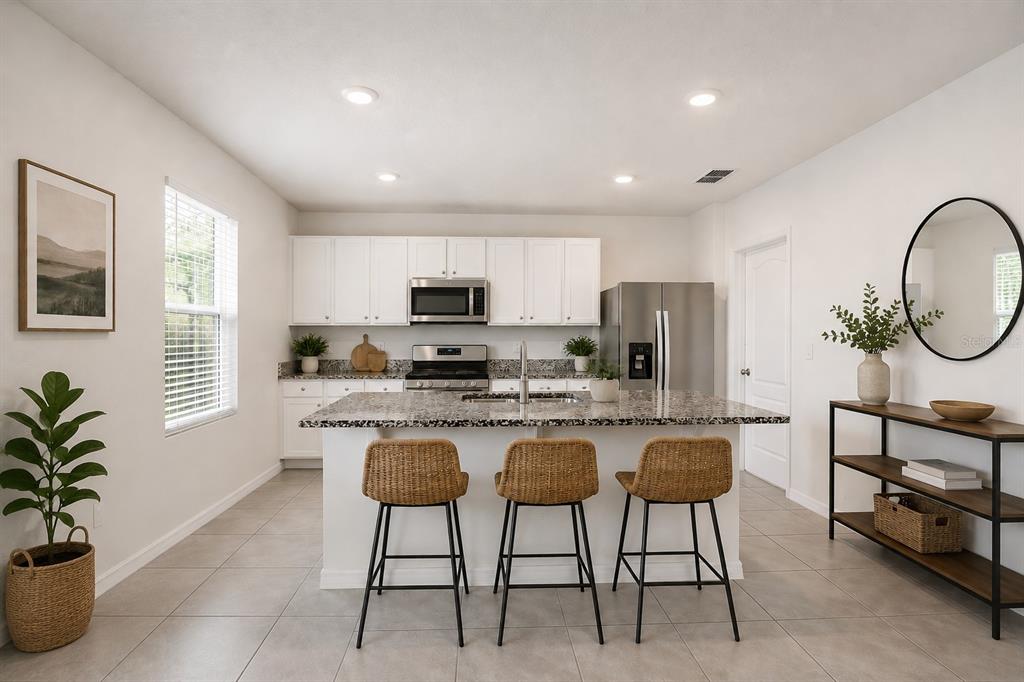 A kitchen features white cabinets, granite countertops, a central island with three stools, and tile flooring — 531 LAZIO CIRCLE, DEBARY, FL
