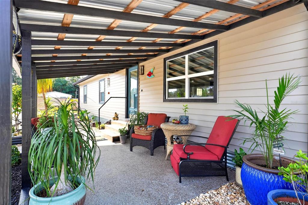 A covered porch features a concrete floor, two red chairs, and several potted plants — 34647 S HAINES CREEK ROAD, LEESBURG, FL