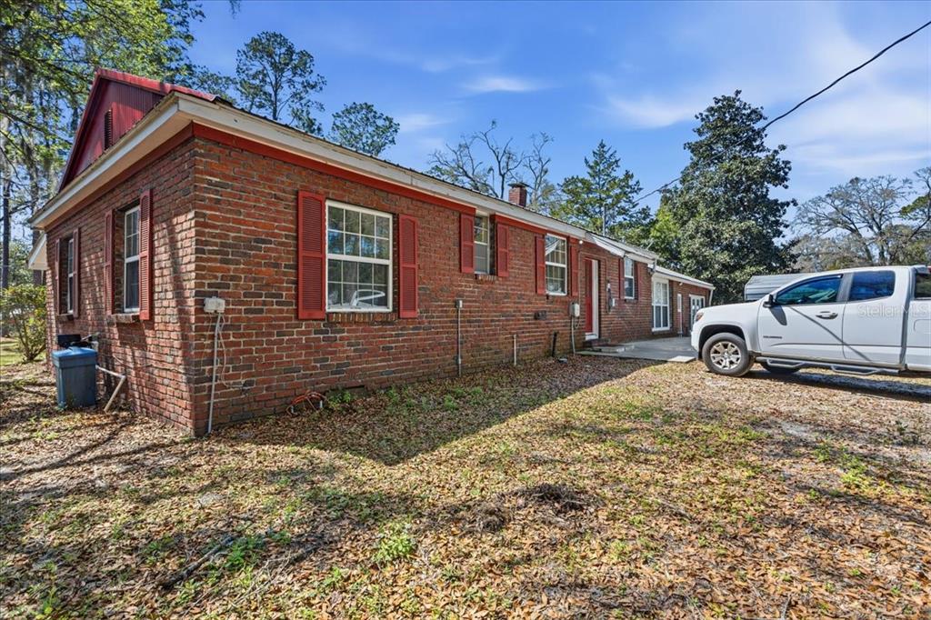 A side view of a single-story brick house with red shutters and a parked truck — 24224 NW 188TH AVENUE, HIGH SPRINGS, FL