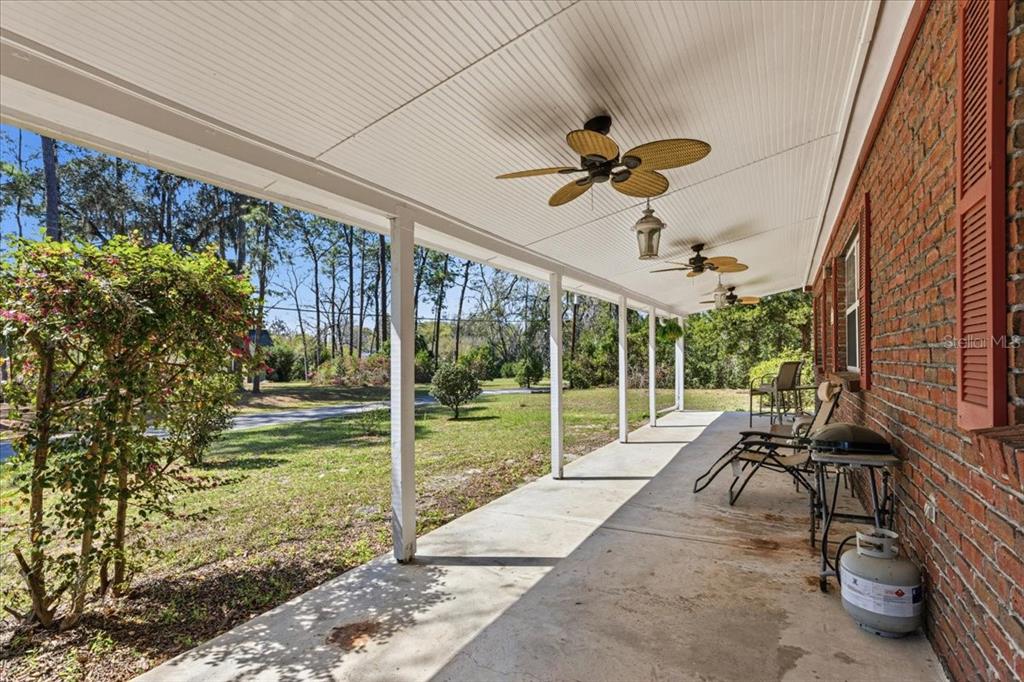 A long, covered concrete porch features white support columns, ceiling fans, and brick exterior walls — 24224 NW 188TH AVENUE, HIGH SPRINGS, FL