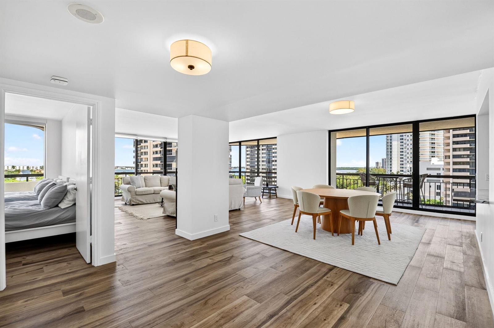 An open-concept living and dining area with wood-look flooring and floor-to-ceiling windows overlooking buildings — 4000 N Ocean Drive # 703, Singer Island FL 33404, SINGER ISLAND, FL