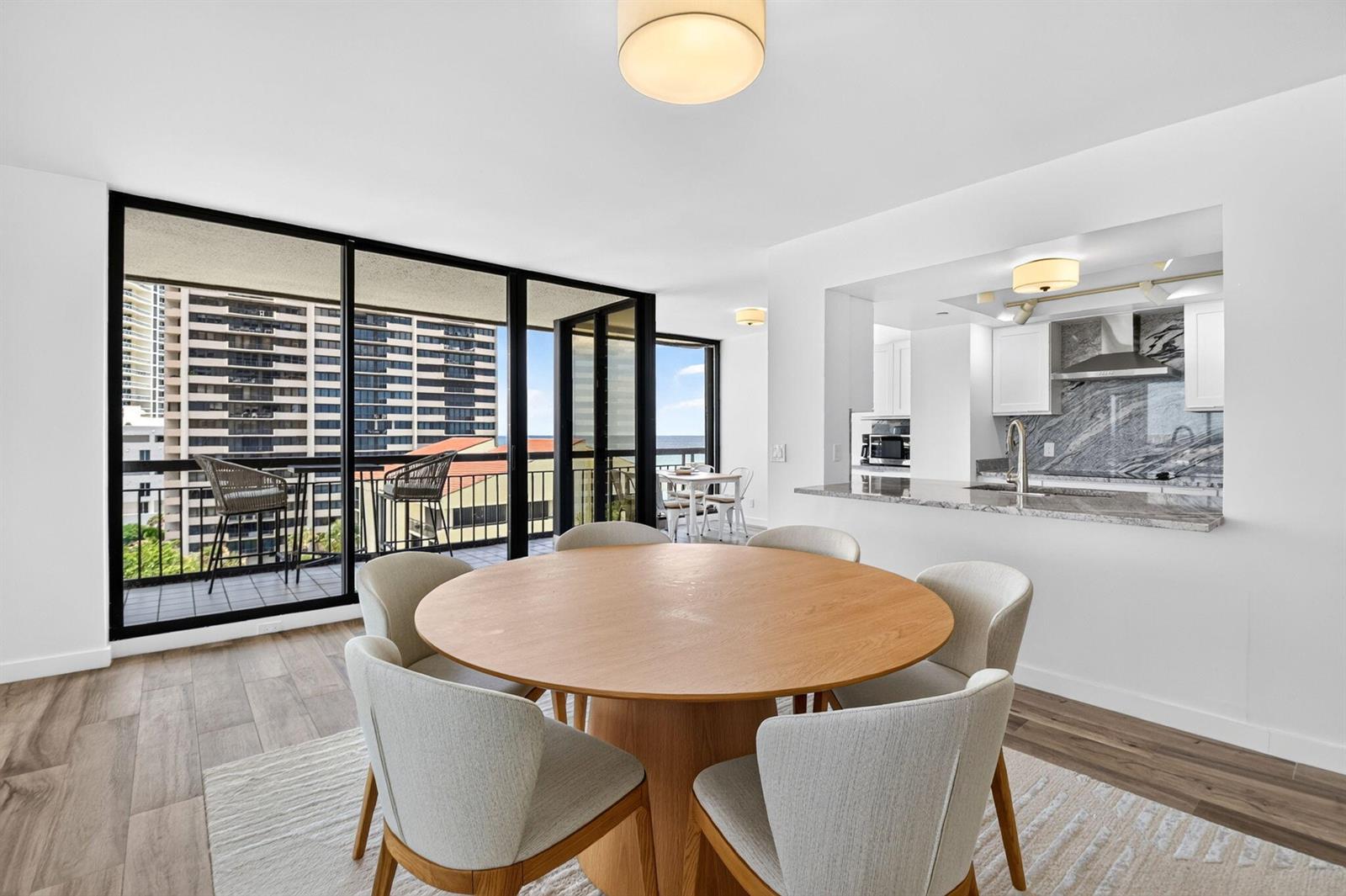 A dining area with a round wooden table and chairs sits beside a modern kitchen — 4000 N Ocean Drive # 703, Singer Island FL 33404, SINGER ISLAND, FL