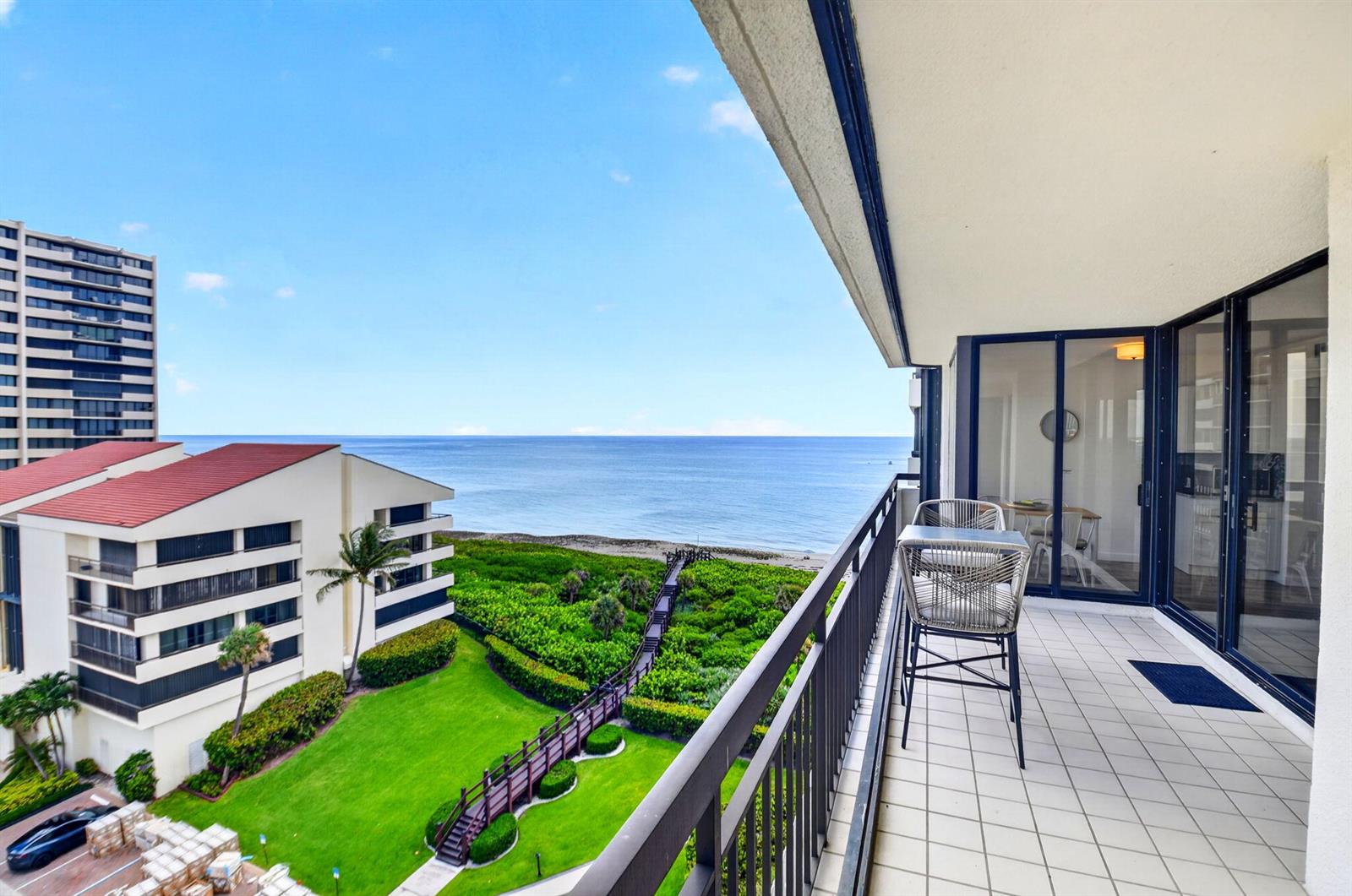 A balcony with outdoor seating overlooks a grassy lawn, a wooden walkway, and the ocean — 4000 N Ocean Drive # 703, Singer Island FL 33404, SINGER ISLAND, FL
