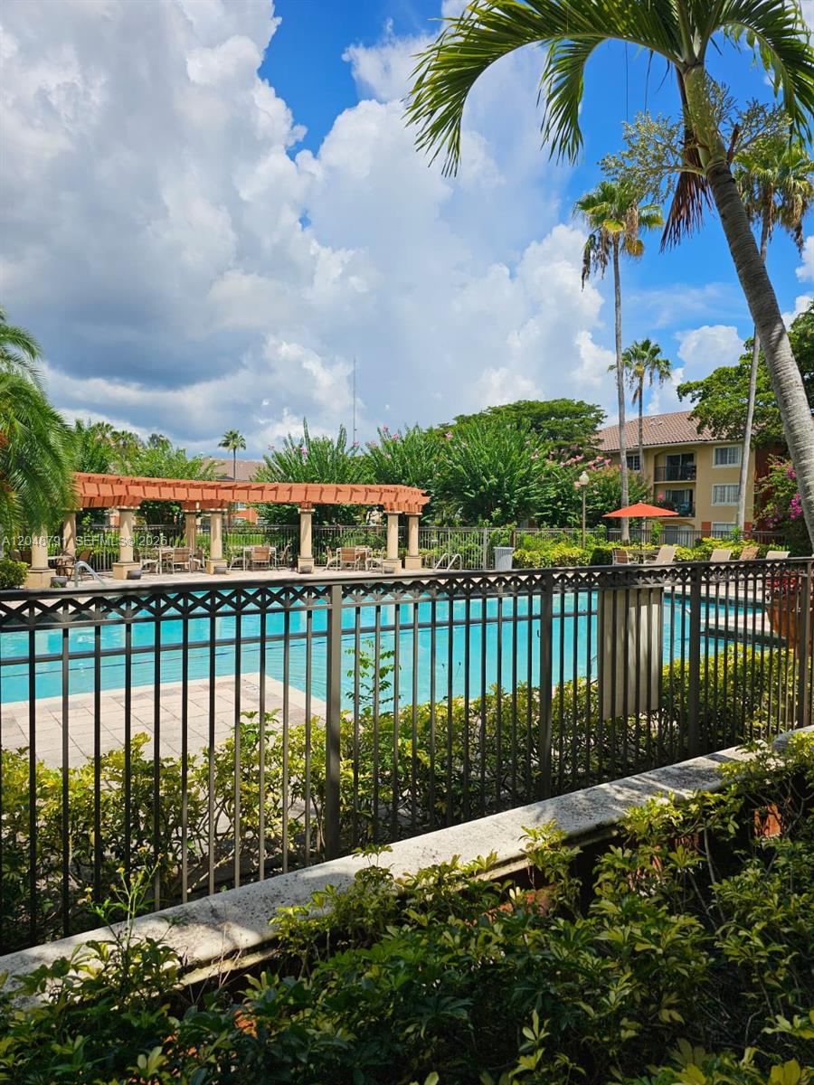 A swimming pool area features a wooden pergola, metal fencing, and surrounding palm trees — WEST PALM BEACH, FL