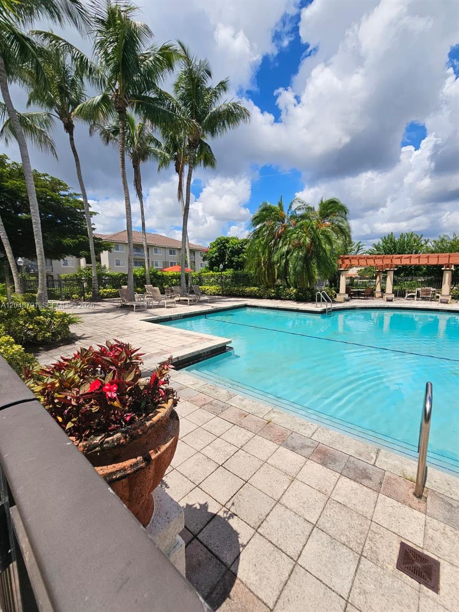 A swimming pool with a tiled deck, palm trees, and a pergola under a cloudy sky — WEST PALM BEACH, FL