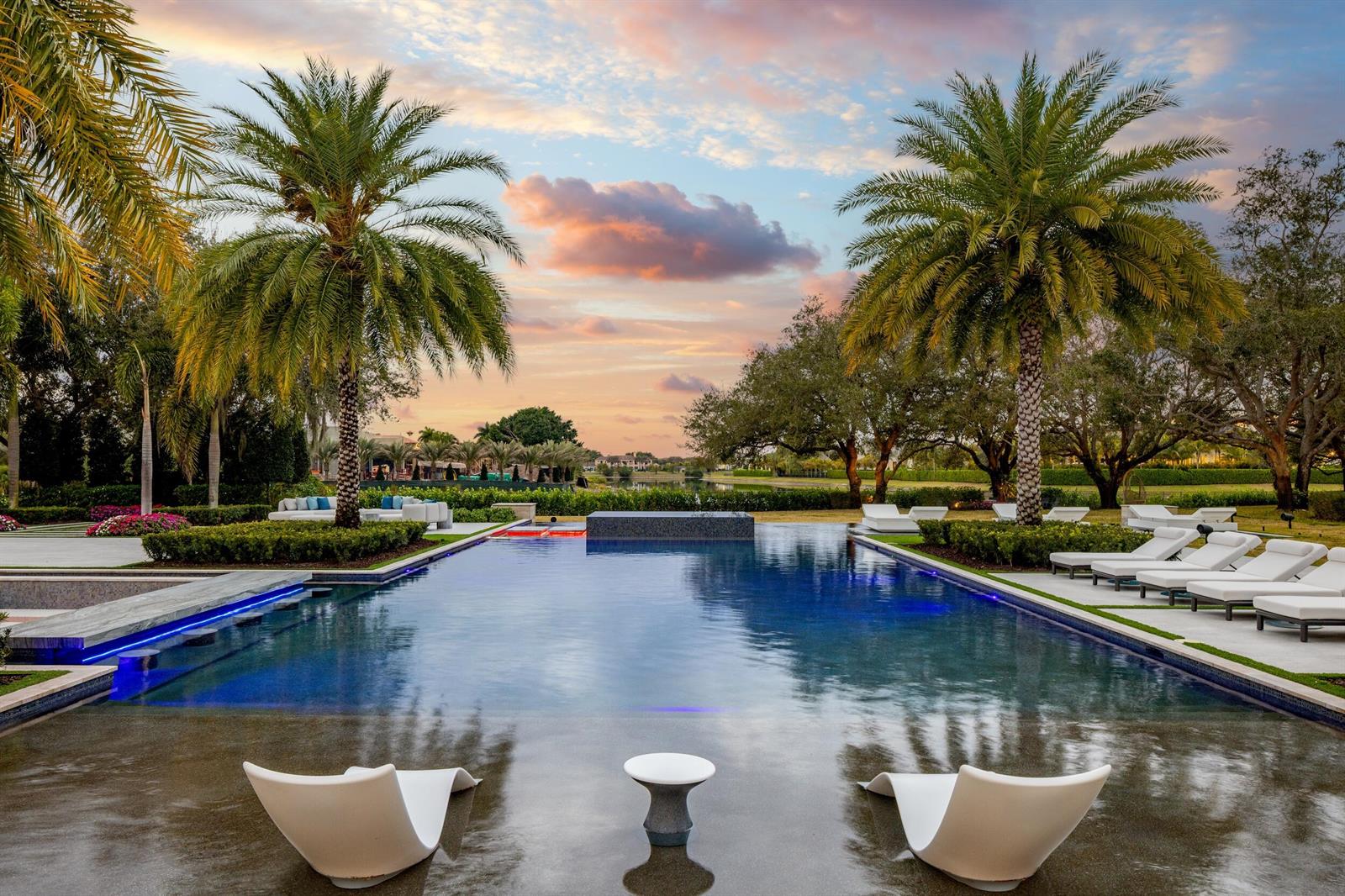 A swimming pool with lounge chairs sits in a backyard with palm trees at sunset — 16191 Quiet Vista Circle, Delray Beach FL 33446, DELRAY BEACH, FL