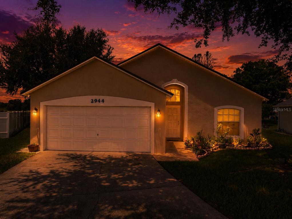 A single-story house with a two-car garage and a landscaped front yard at sunset — 2944 COOL BREEZE CIRCLE, ST CLOUD, FL