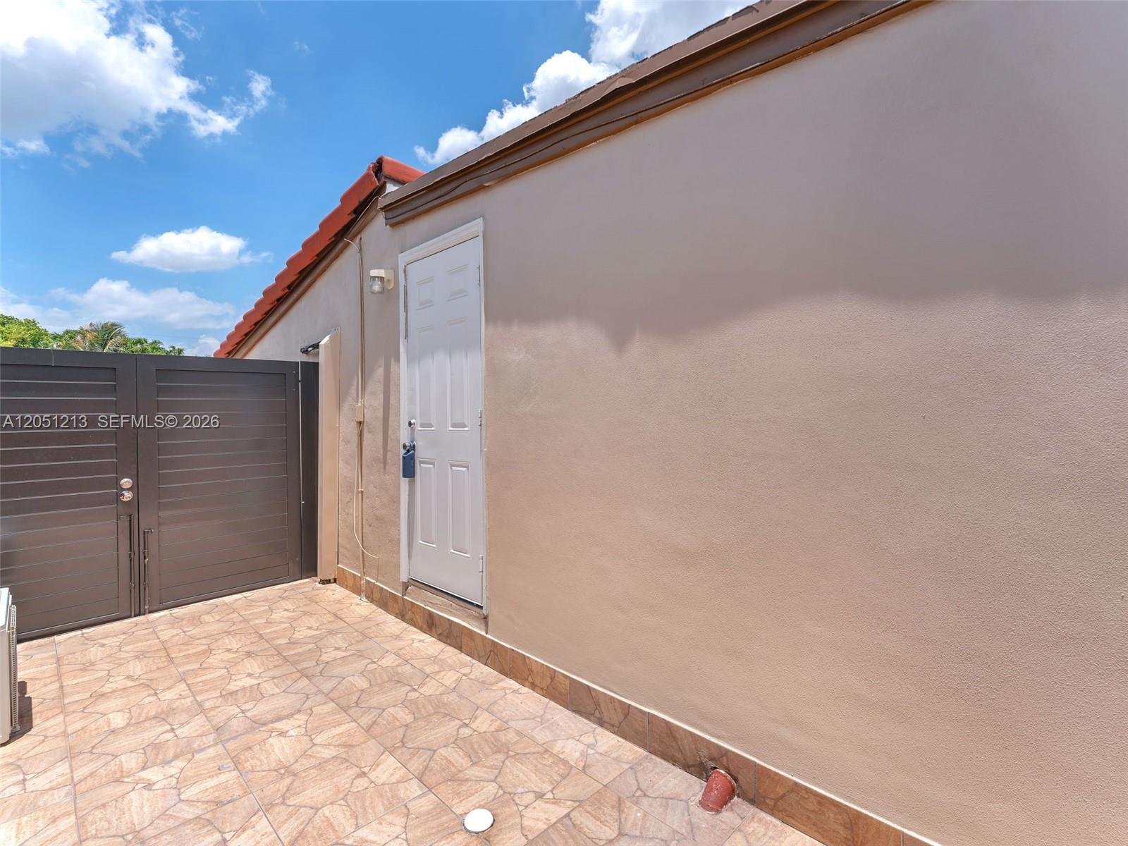 A white door is set into a beige exterior wall next to a dark gate — MIAMI, FL