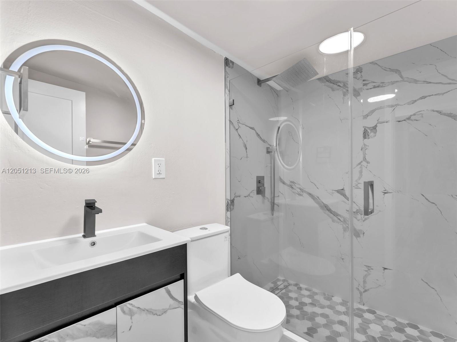 A modern bathroom features a marble-tiled walk-in shower, a floating vanity, and a backlit mirror — MIAMI, FL