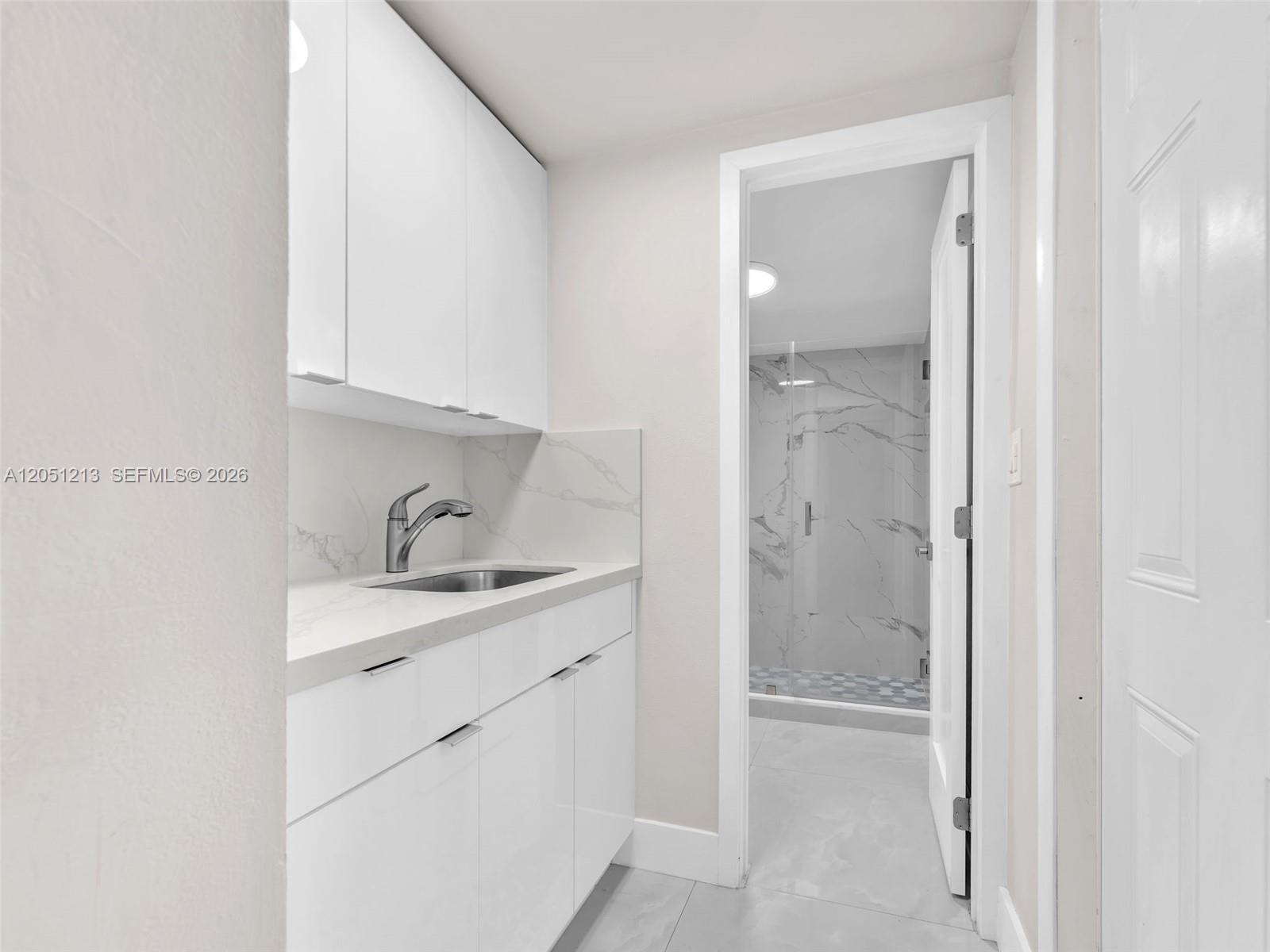 A white vanity with a sink and cabinets sits next to a marble-tiled bathroom — MIAMI, FL