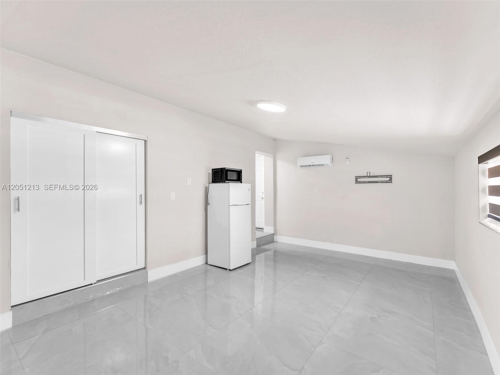 A room with light-colored walls, gray tile flooring, a white refrigerator, and sliding closet doors — MIAMI, FL