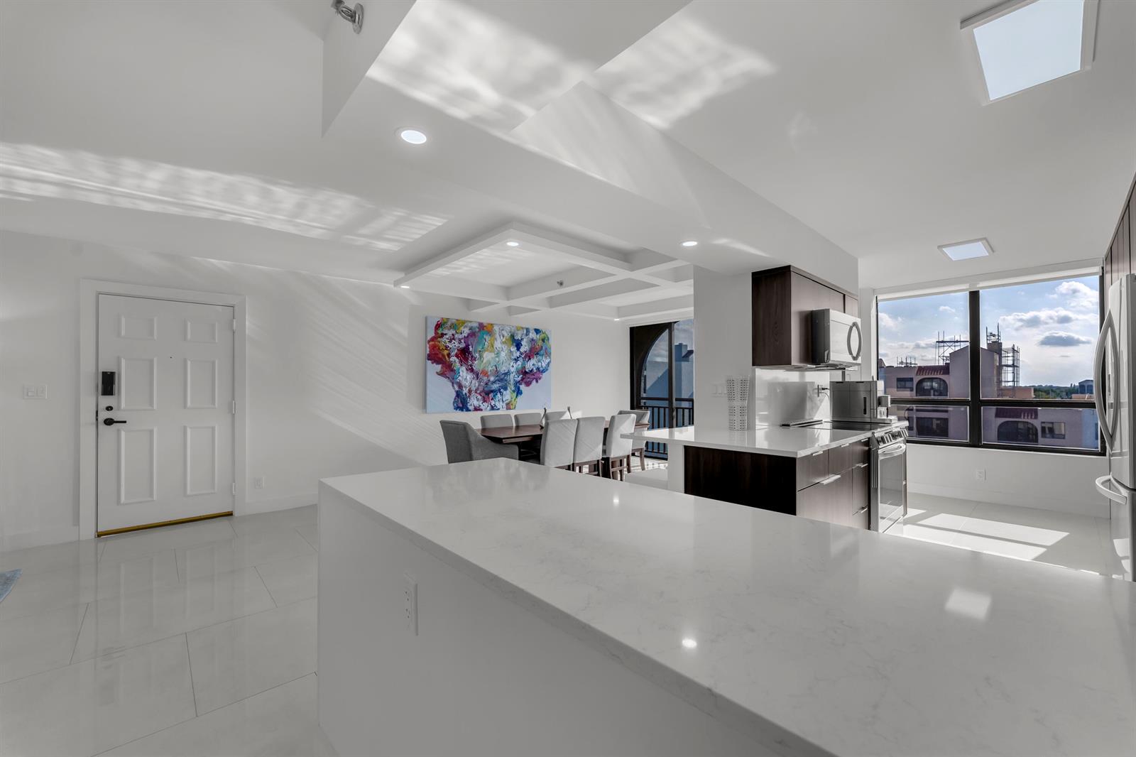 A modern kitchen and dining area feature white countertops, dark cabinetry, and large windows — 7178 Promenade Drive # 801b, Boca Raton FL 33433, BOCA RATON, FL