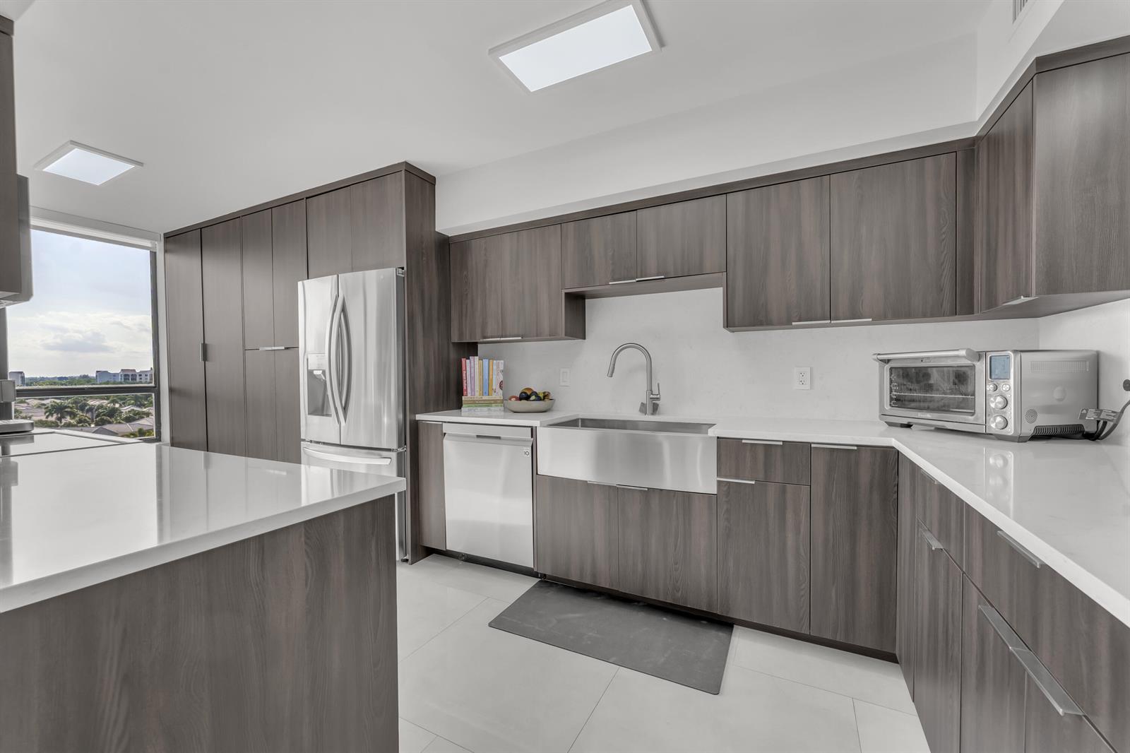 A modern kitchen features dark wood cabinets, white countertops, a farmhouse sink, and stainless appliances — 7178 Promenade Drive # 801b, Boca Raton FL 33433, BOCA RATON, FL
