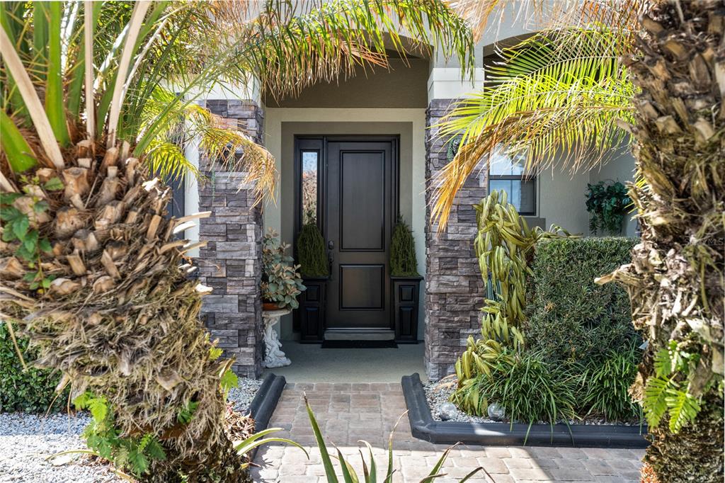 A paved walkway leads to a dark front door flanked by stone pillars and palms — 3816 BOWFIN TRAIL, KISSIMMEE, FL