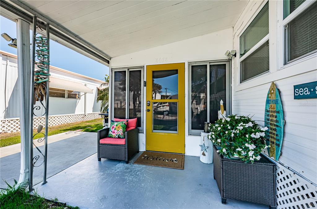 A covered porch features a yellow front door, a wicker chair, and a potted plant — 8678 44TH AVENUE N UNIT 62, ST PETERSBURG, FL