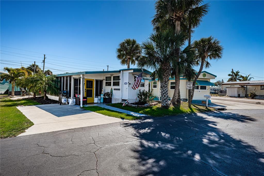 A white mobile home with a yellow door and a concrete driveway sits under palm trees — 8678 44TH AVENUE N UNIT 62, ST PETERSBURG, FL