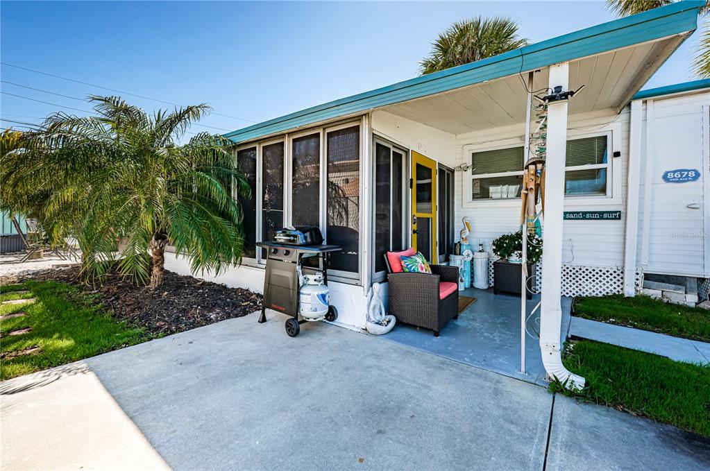 A concrete patio leads to a screened-in porch and a yellow door on a home — 8678 44TH AVENUE N UNIT 62, ST PETERSBURG, FL