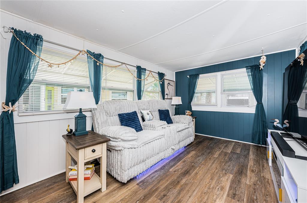 A living room features a light gray sofa, wood-look flooring, and dark blue accent walls — 8678 44TH AVENUE N UNIT 62, ST PETERSBURG, FL