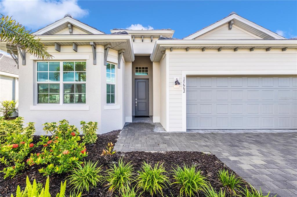 The exterior of a single-story house features a gray front door, garage, and landscaped yard — 17662 SANTORINI COURT, VENICE, FL
