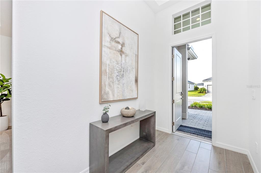 An entryway features a gray console table, abstract wall art, and an open front door — 17662 SANTORINI COURT, VENICE, FL