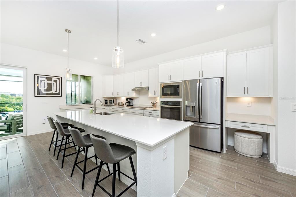 A modern kitchen features white cabinetry, stainless steel appliances, a large island, and tile flooring — 17662 SANTORINI COURT, VENICE, FL