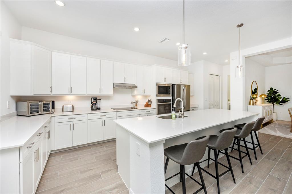 A modern kitchen features white cabinetry, quartz countertops, a large island, and wood-look tile flooring — 17662 SANTORINI COURT, VENICE, FL