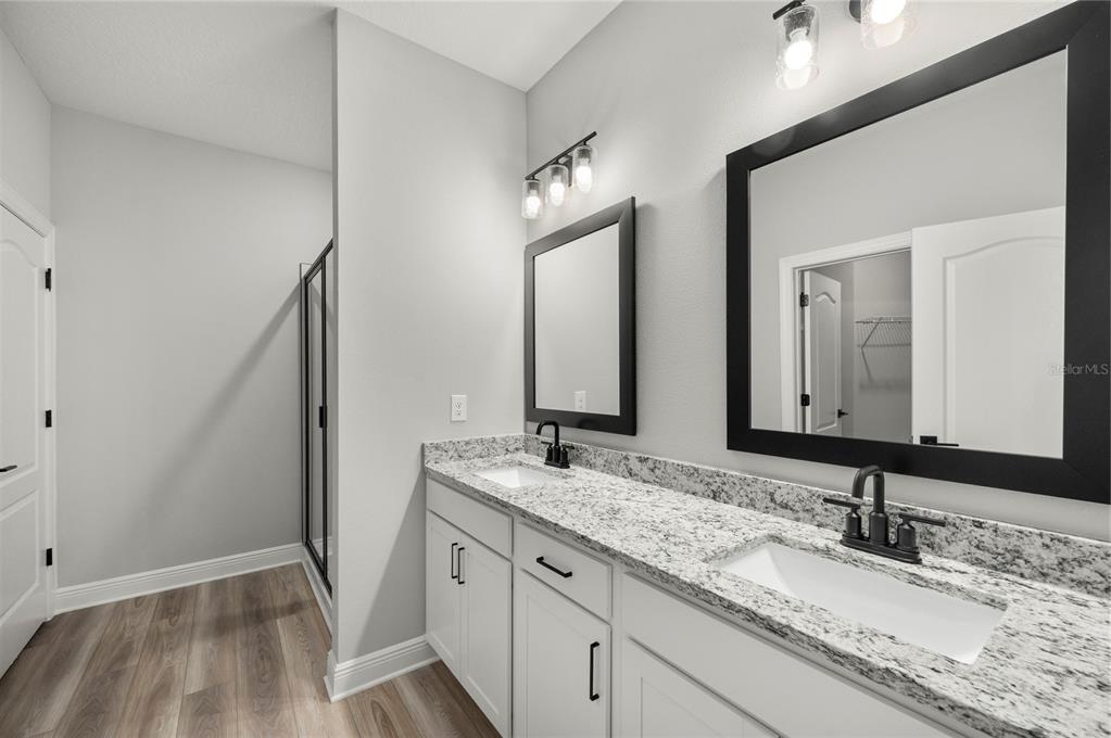 A bathroom features a double vanity with granite countertops, white cabinets, and two framed mirrors — 7752 SOMERSWORTH DRIVE, KISSIMMEE, FL