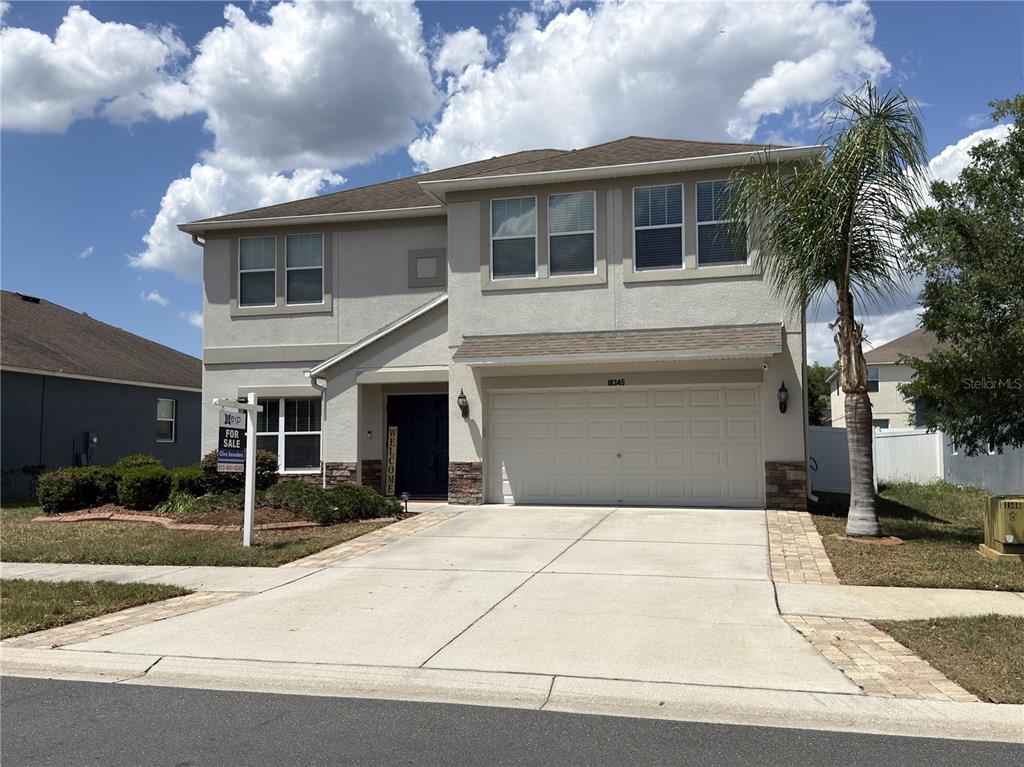 A two-story suburban house with a beige stucco exterior, a two-car garage, and a palm tree — 18345 FISH LOOP, LAND O LAKES, FL