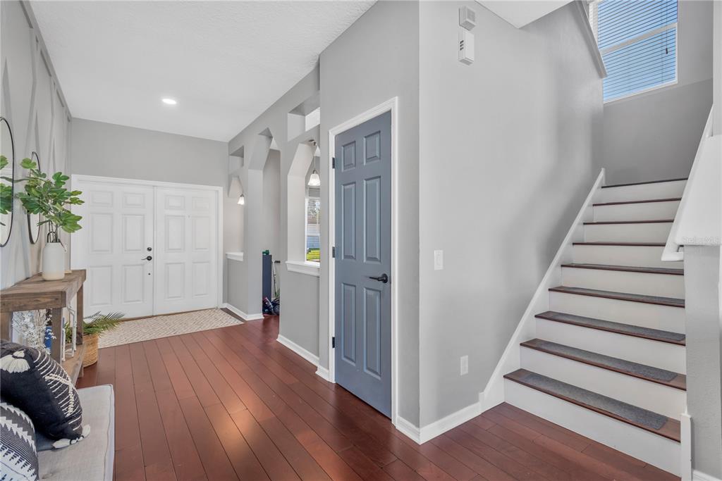 An entryway features hardwood floors, a blue door, and a staircase with white risers — 18345 FISH LOOP, LAND O LAKES, FL