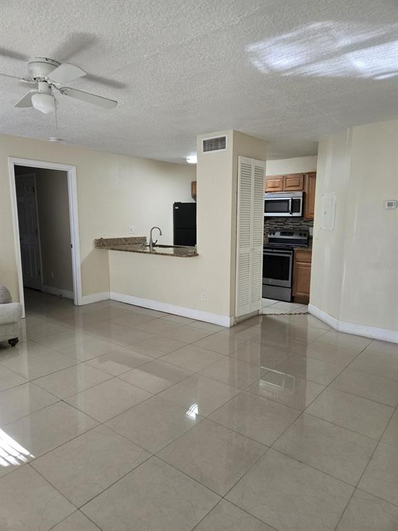 An open-concept kitchen features granite countertops, stainless steel appliances, and light-colored tile flooring — 4756 WALDEN CIRCLE UNIT 11, ORLANDO, FL