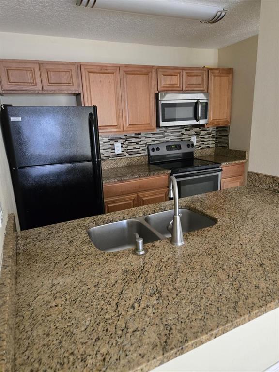 A kitchen features wood cabinets, granite countertops, a black refrigerator, and stainless steel appliances — 4756 WALDEN CIRCLE UNIT 11, ORLANDO, FL