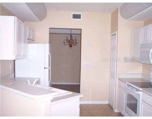 A kitchen with white cabinets, white appliances, and a pass-through opening to a dining area — 4484 STREAMSIDE COURT UNIT 1503, SARASOTA, FL
